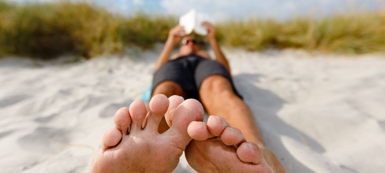 Ein Mann liegt am Ostseestrand und liest ein Buch.