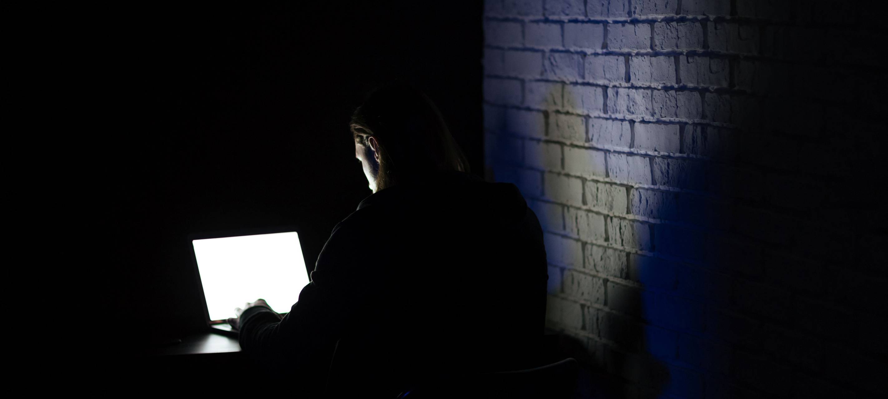 Ein Mann sitzt im dunkeln an einem Laptop
