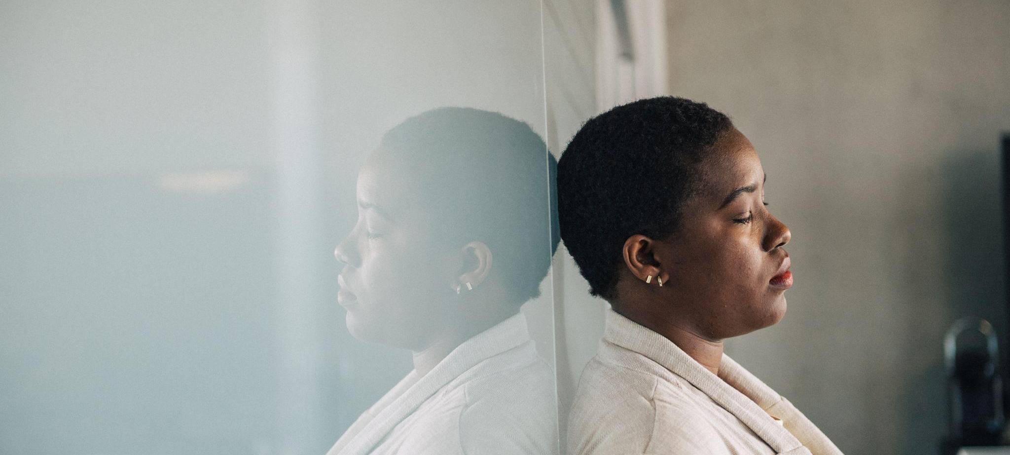 Eine junge Frau lehnt nachdenklich an einer Glaswand