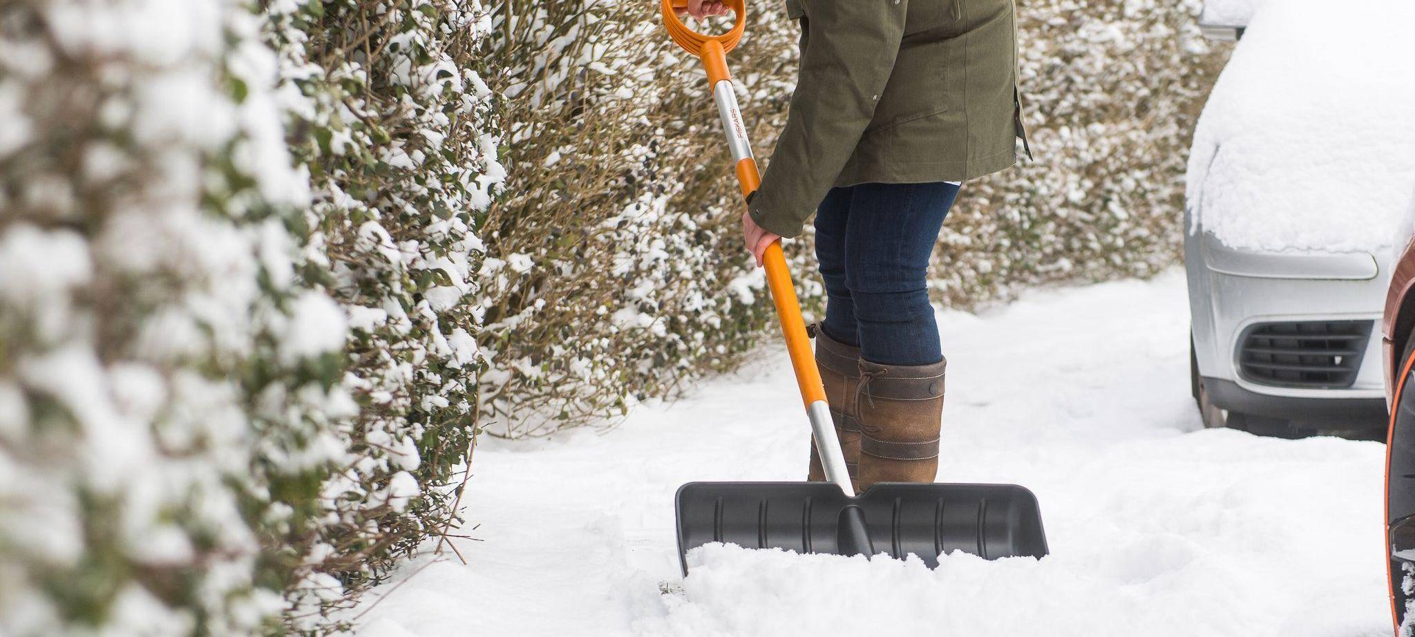 Eine Frau schippt Schnee auf dem Gehweg vor ihrem Haus