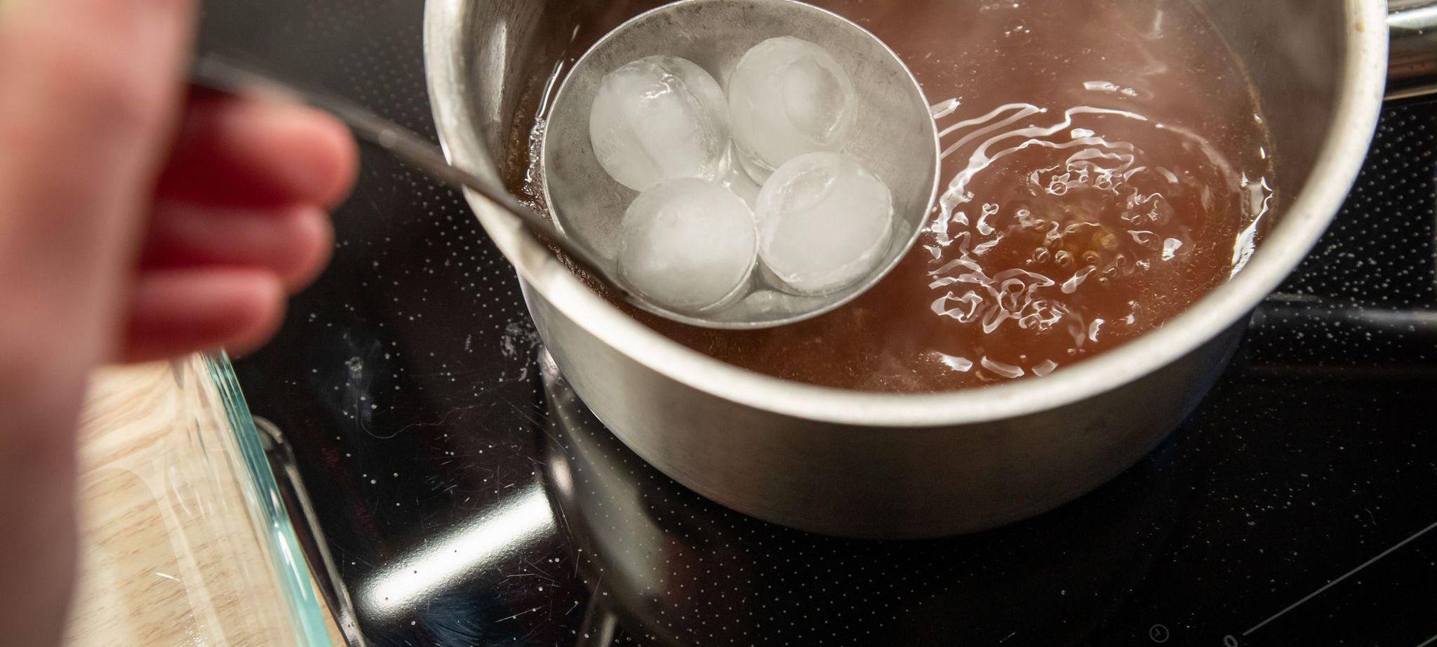 Eiswürfel in einer Suppenkelle werden über Brühe gehalten