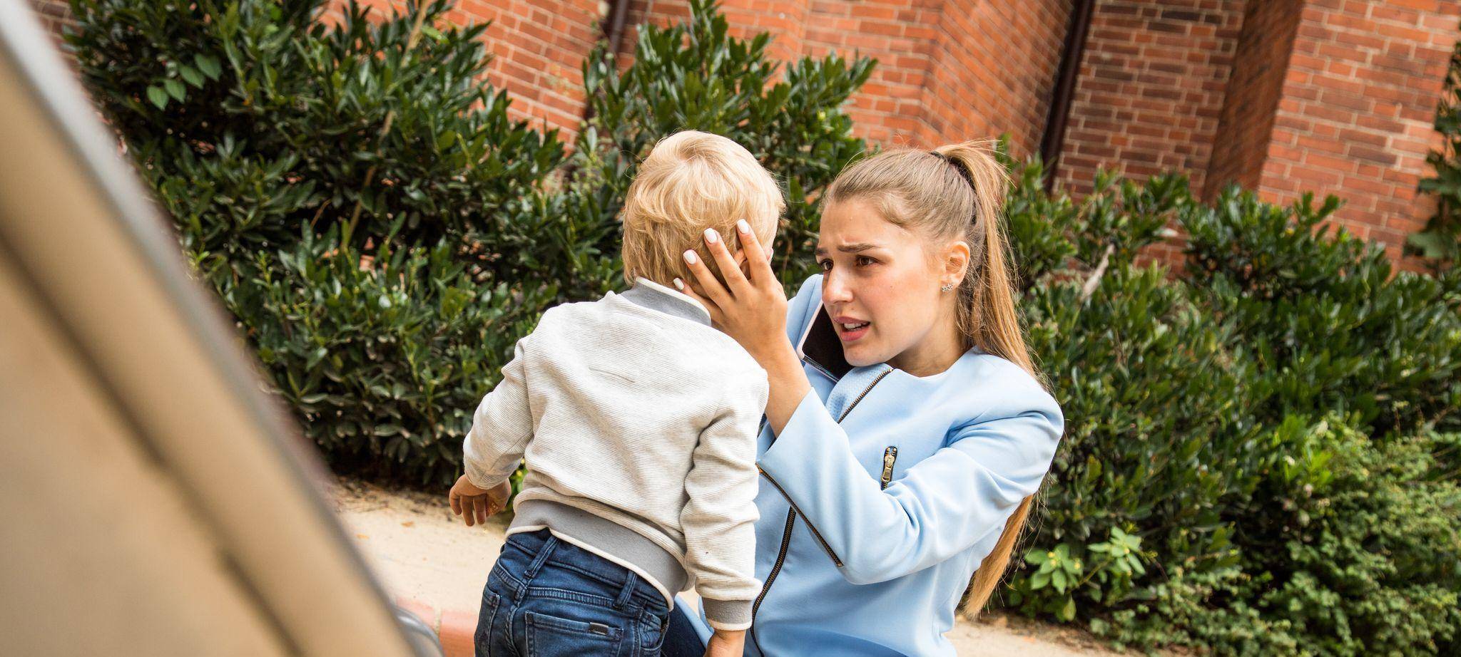 Mutter hält auf dem Spielplatz besorgt den Kopf ihres Kindes