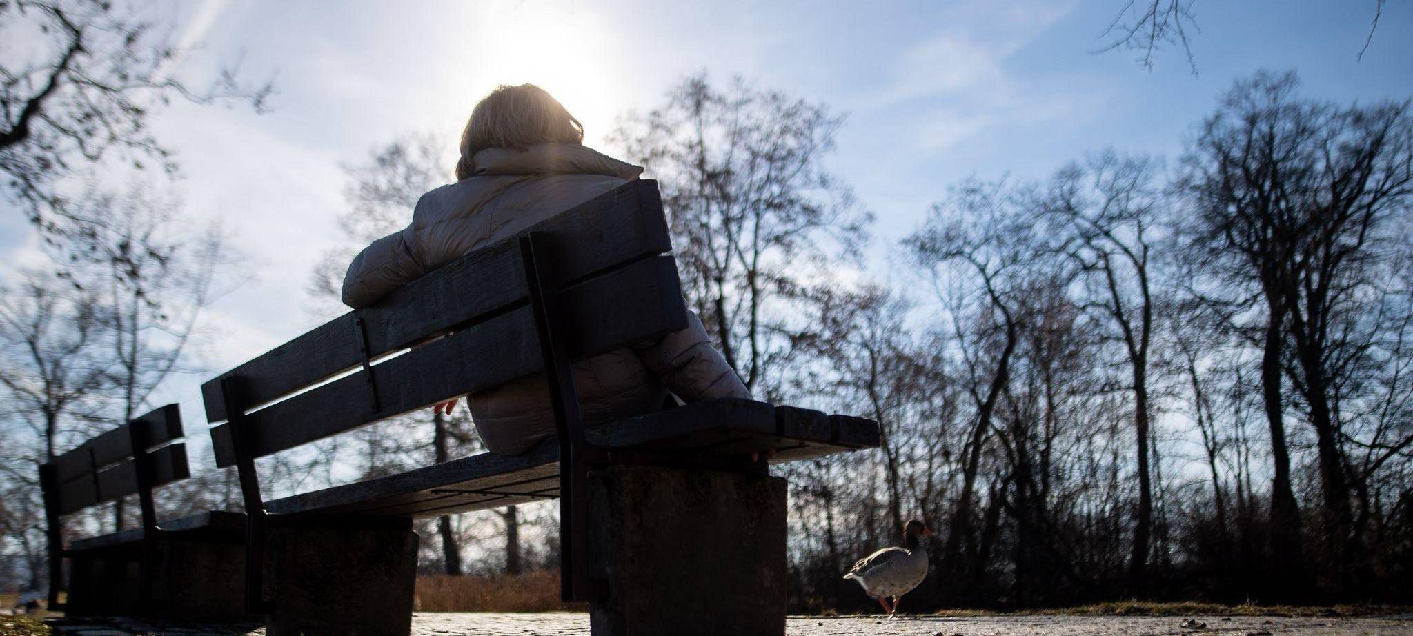 Eine Frau sitzt neben kahlen Bäumen in der Sonne